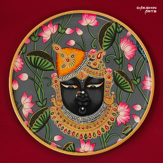 A Pichwai wooden wall plate with a painting of Srinathji surrounded by pink lotus flowers on a gray background- Dakshin Arts