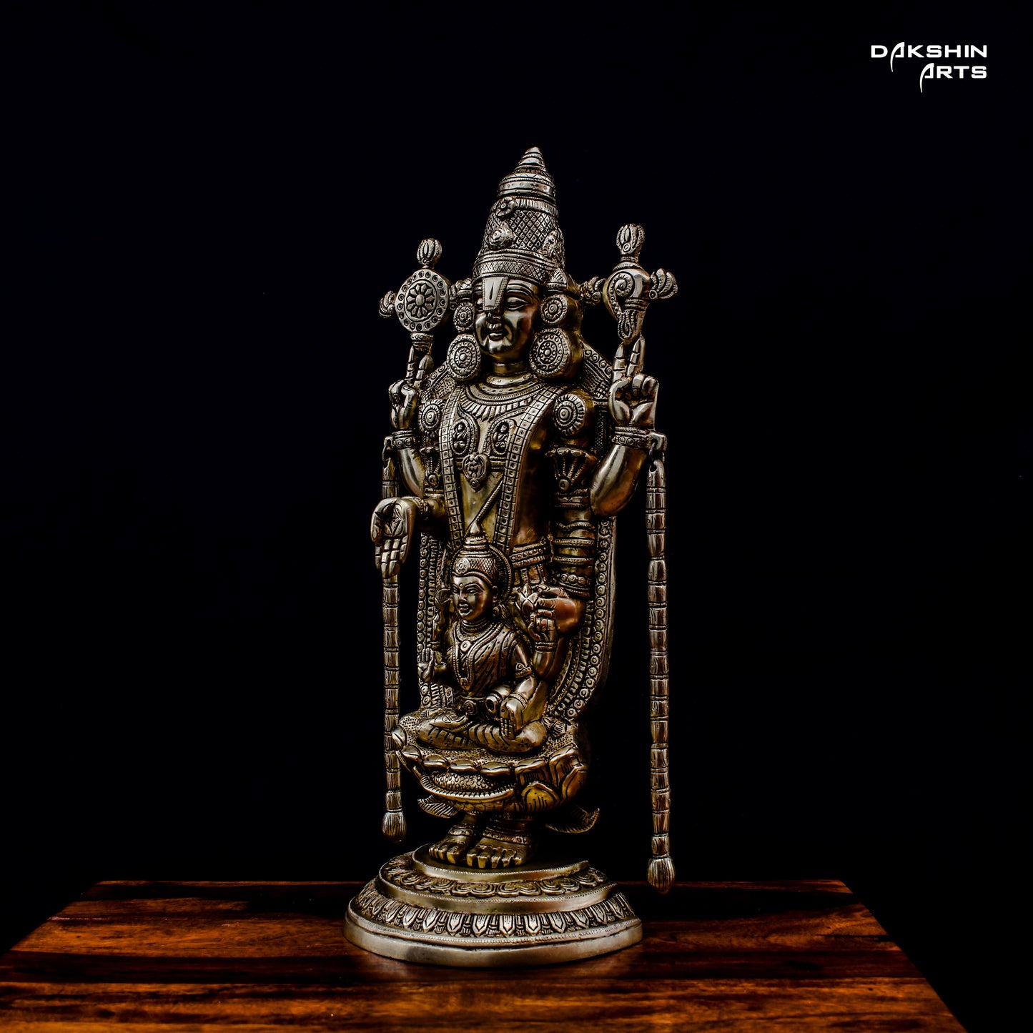 A brass Balaji Padmavati stands on a wooden surface against a black background- Dakshin Arts