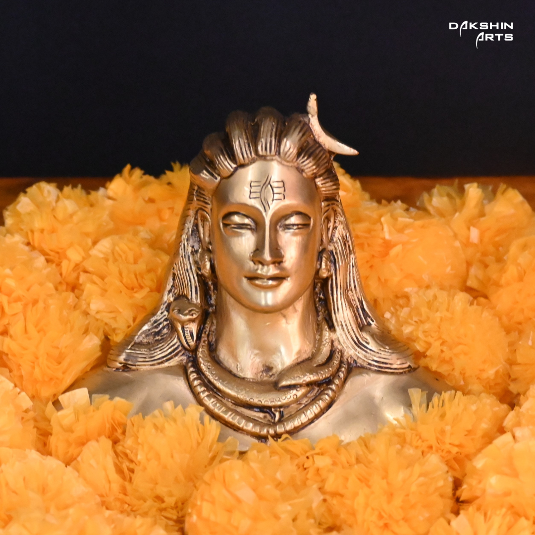 Brass adiyogi with closed eyes, featuring a crescent on the head and surrounded with Marigold Flower, against a dark background.