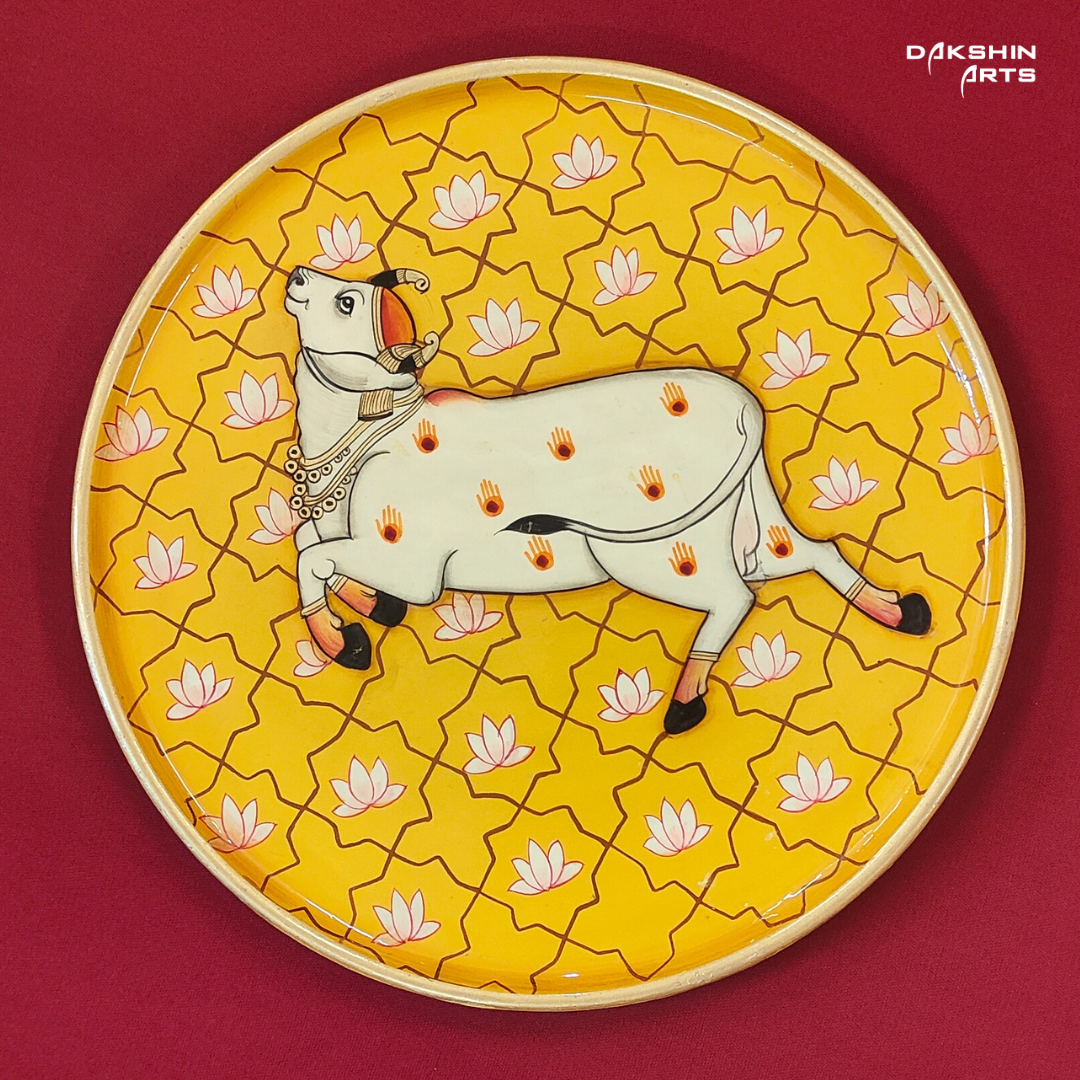 A decorative Pichwai wooden wall plate featuring a white cow on a vibrant yellow background with lotus - Dakshin Arts