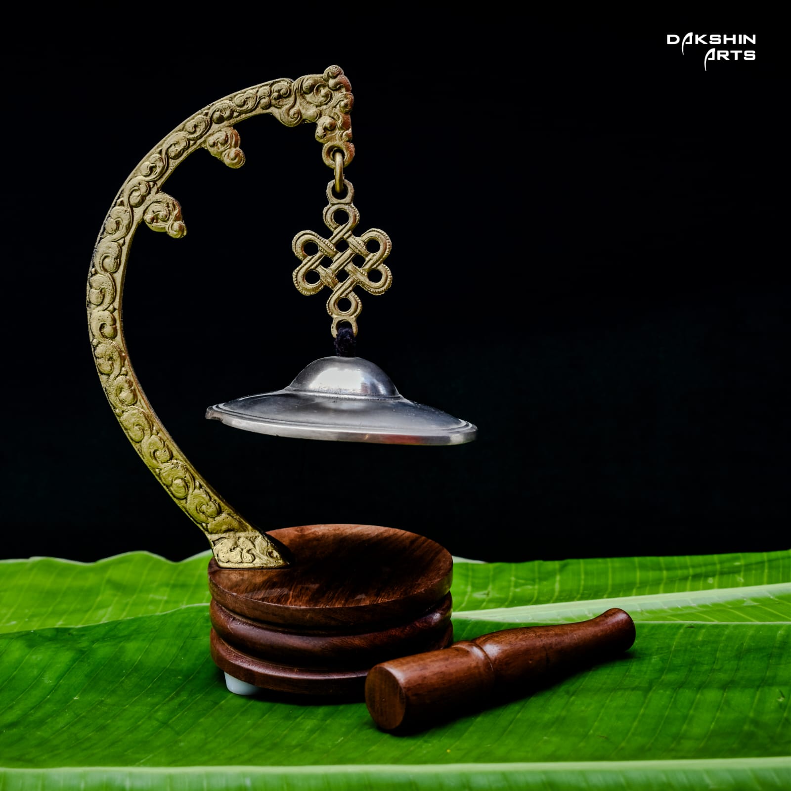 An intricately designed brass meditation gong on a wooden base rests on a banana leaf- Dakshin Arts