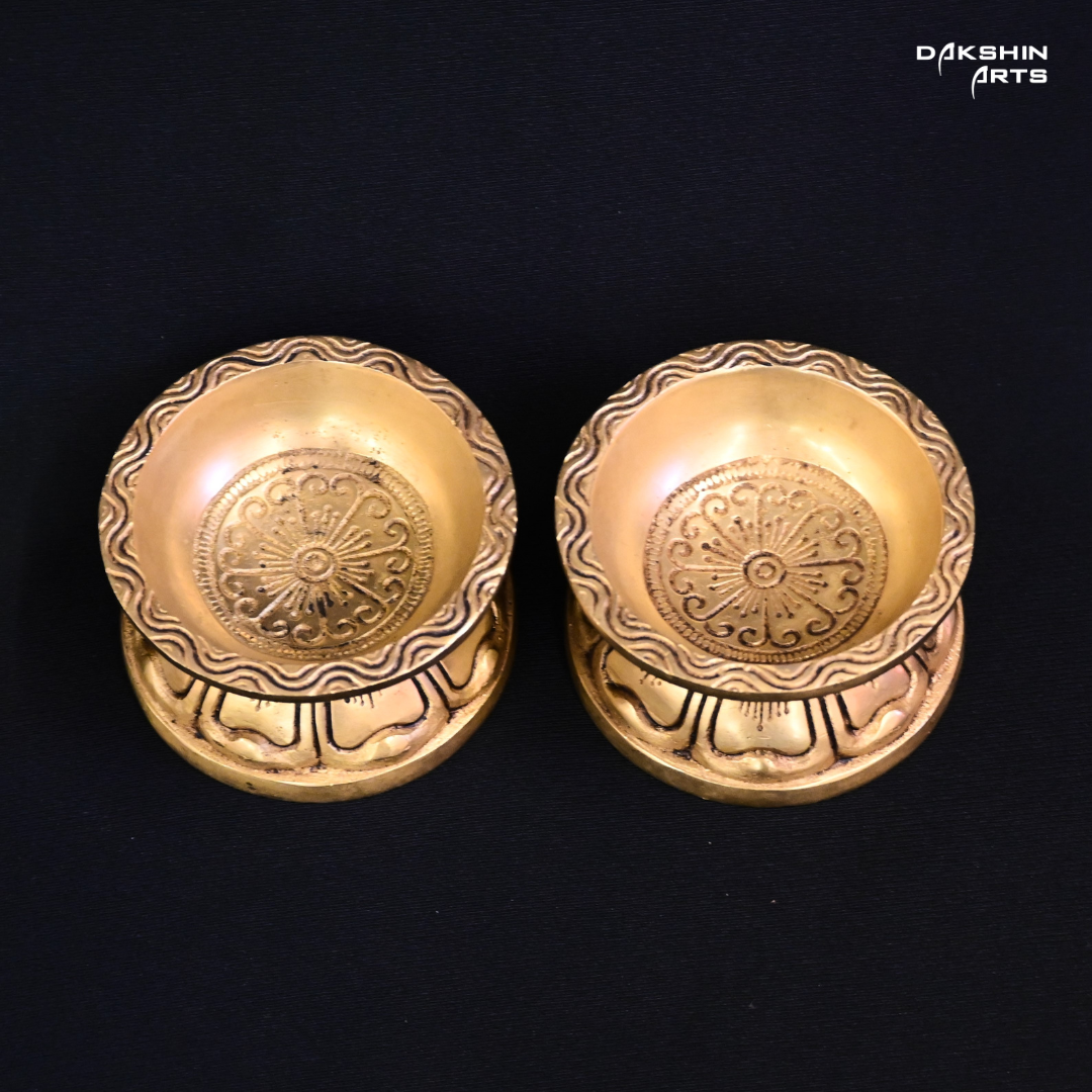 Two ornate brass diyas with engraved designs on a black background, exuding an elegant tone - Dakshin Arts