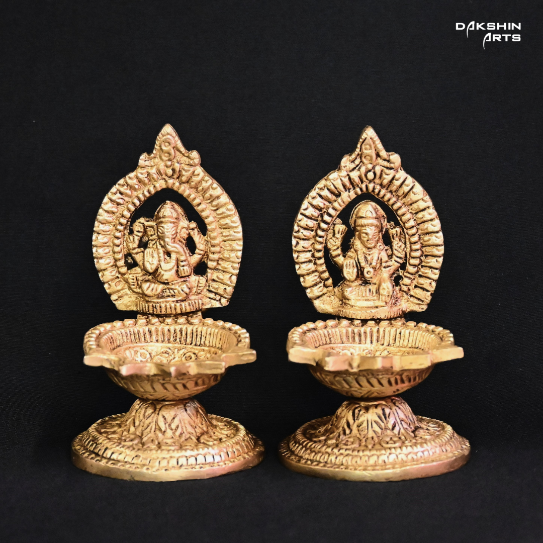 Two ornate brass oil lamps with intricate carvings of Ganesha and Laxmi - Dakshin Arts