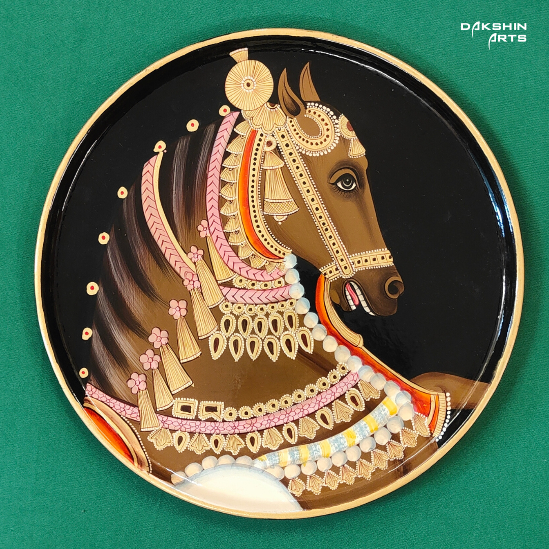 A decorative Pichwai wooden plate with an intricately painted horse head with pink and gold ornaments on a black background - Dakshin Arts