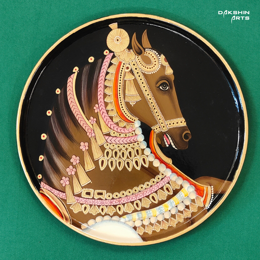 A decorative Pichwai wooden plate with an intricately painted horse head with pink and gold ornaments on a black background - Dakshin Arts