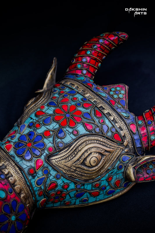 Colorful decorative brass Nandi mask with intricate floral patterns in red, blue, and turquoise on a black background- Dakshin Arts
