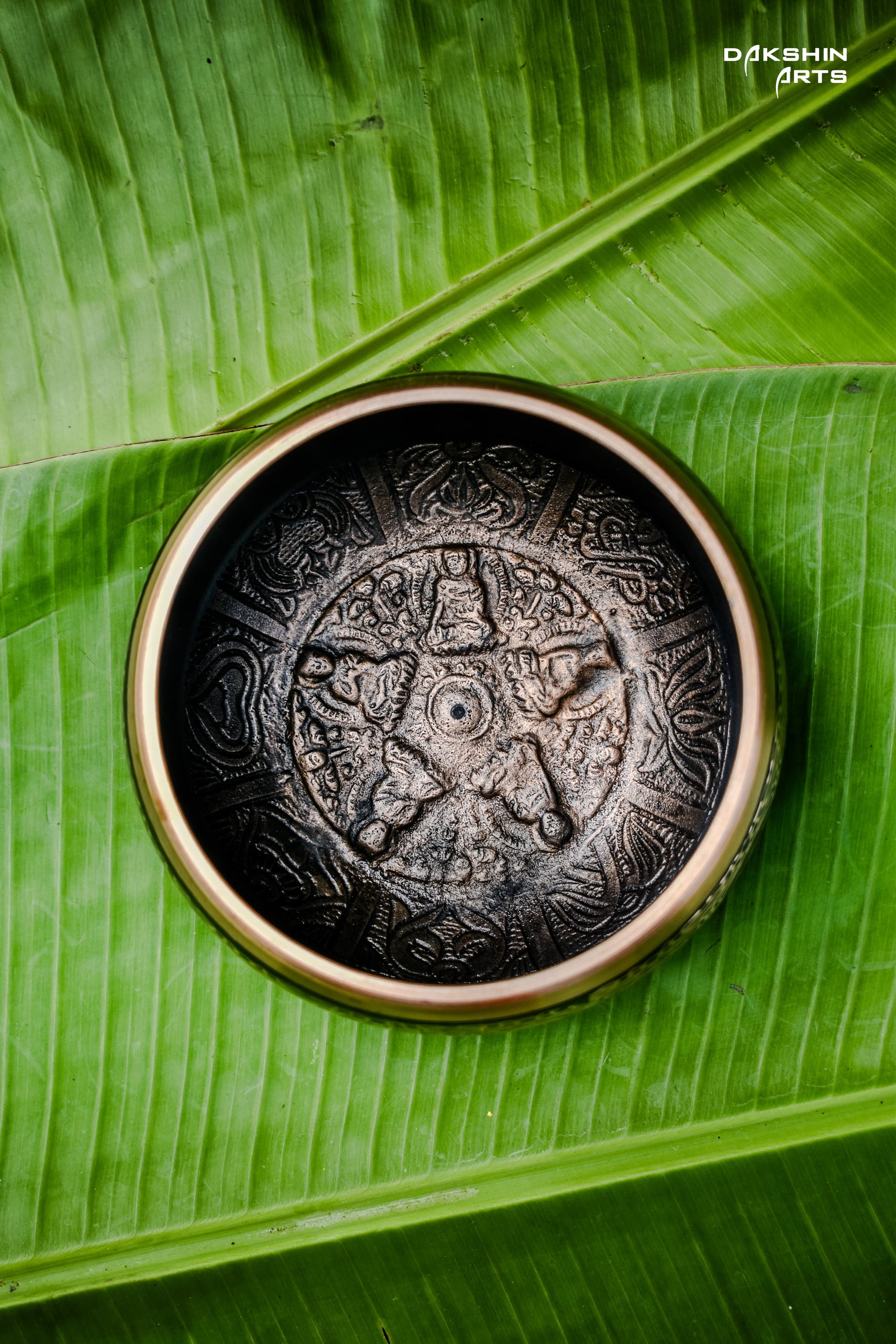 Inner view of a black singing bowl resting on green banana leaves- Dakshin Arts