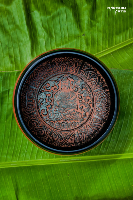 A red singing bowl with intricate patterns sits on vibrant green banana leaves - Dakshin Arts