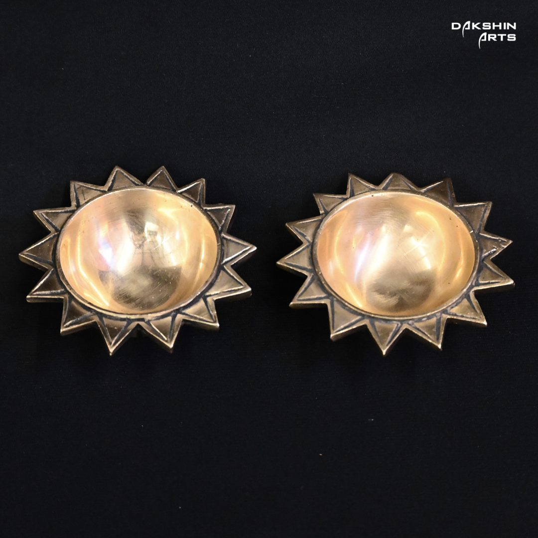 Two brass, sun-shaped diyas with star-like edges on a black background- Dakshin Arts