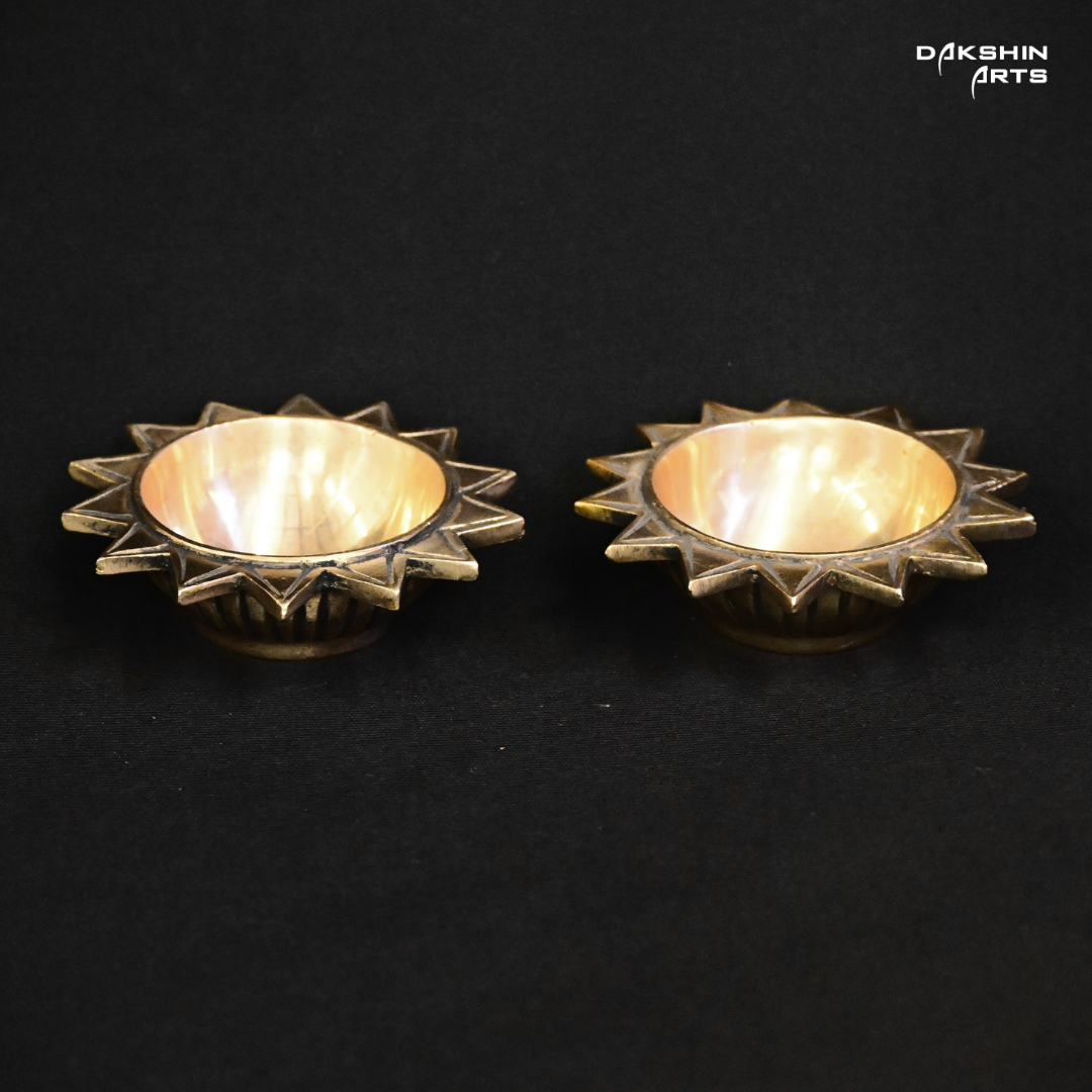 Two brass, sun-shaped diyas with star-like edges on a black background- Dakshin Arts