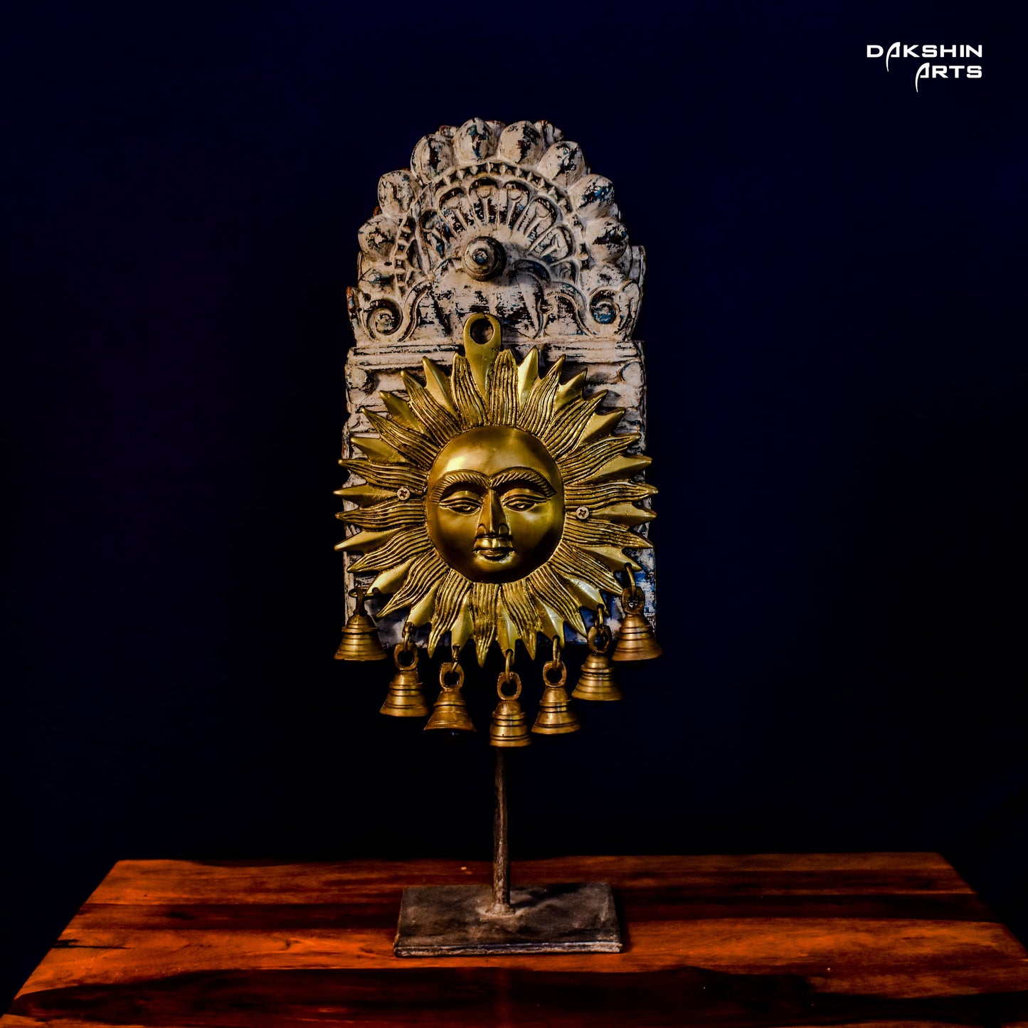 Golden brass sun face with bold rays decor, adorned with multiple small bells, mounted on an ornate wooden arch - Dakshin Arts