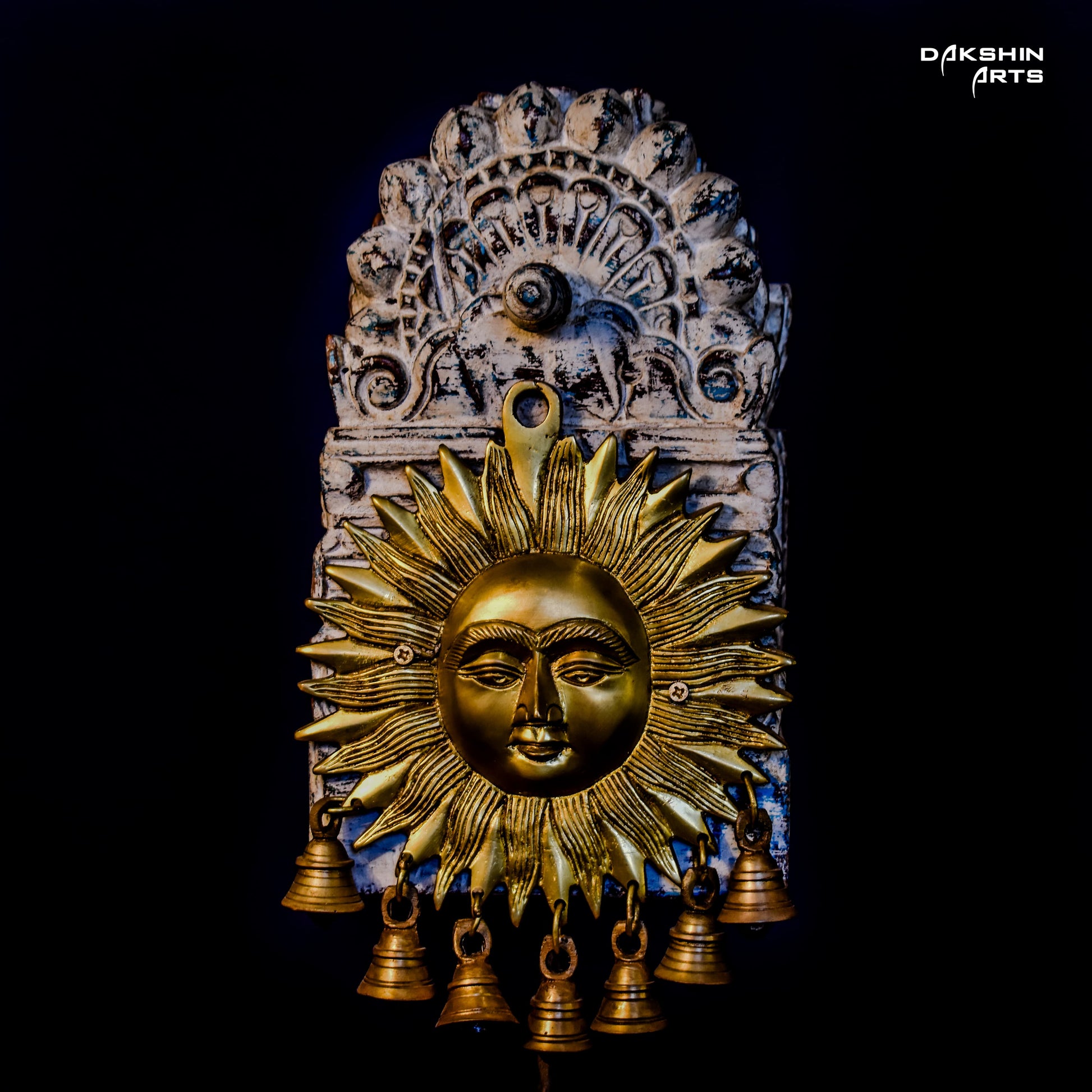 Golden brass sun face with bold rays decor, adorned with multiple small bells, mounted on an ornate wooden arch - Dakshin Arts
