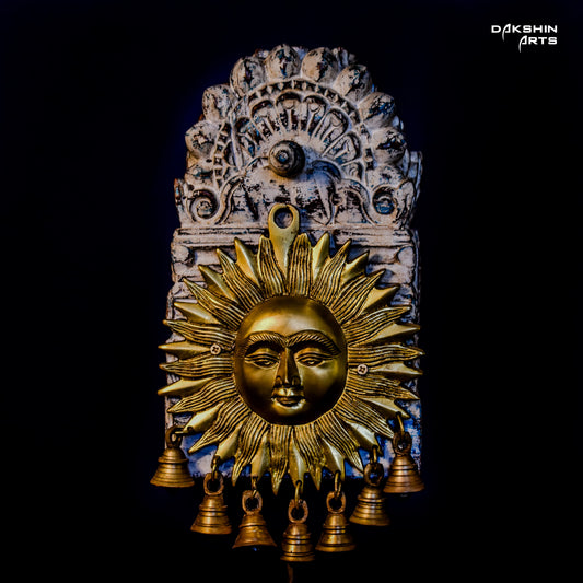 Golden brass sun face with bold rays decor, adorned with multiple small bells, mounted on an ornate wooden arch - Dakshin Arts