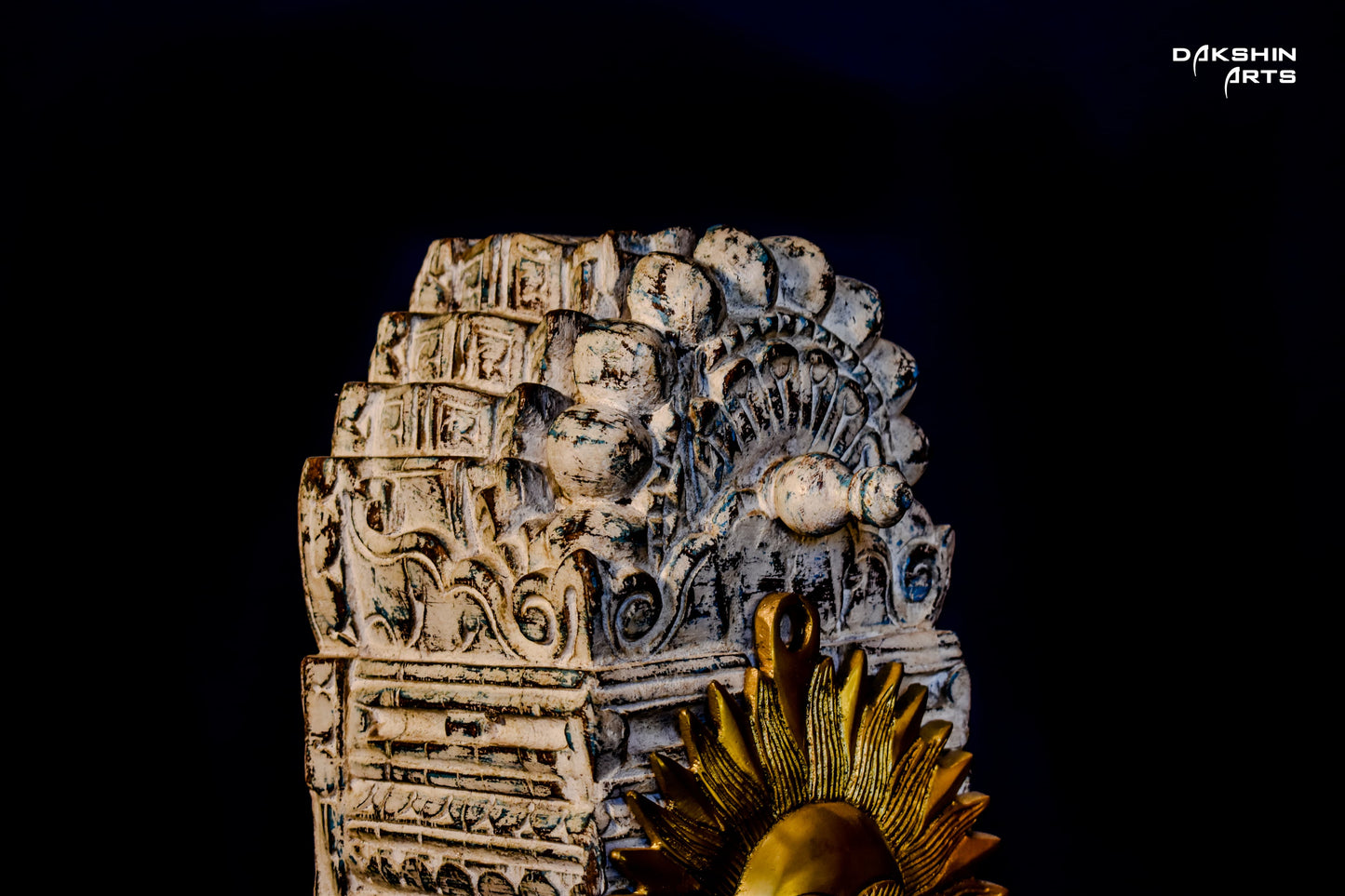 Closeup of a brass sun face with bold rays decor, adorned with multiple small bells, mounted on an ornate wooden arch - Dakshin Arts