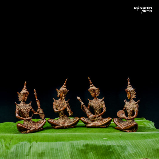 Four intricately carved brass statues of musicians are seated on vibrant green leaves against a black background- Dakshin Arts