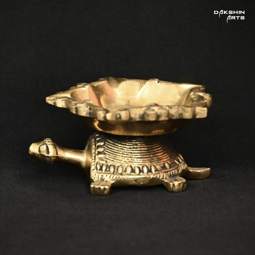 A brass decorative piece in the shape of a turtle with a diya on top.