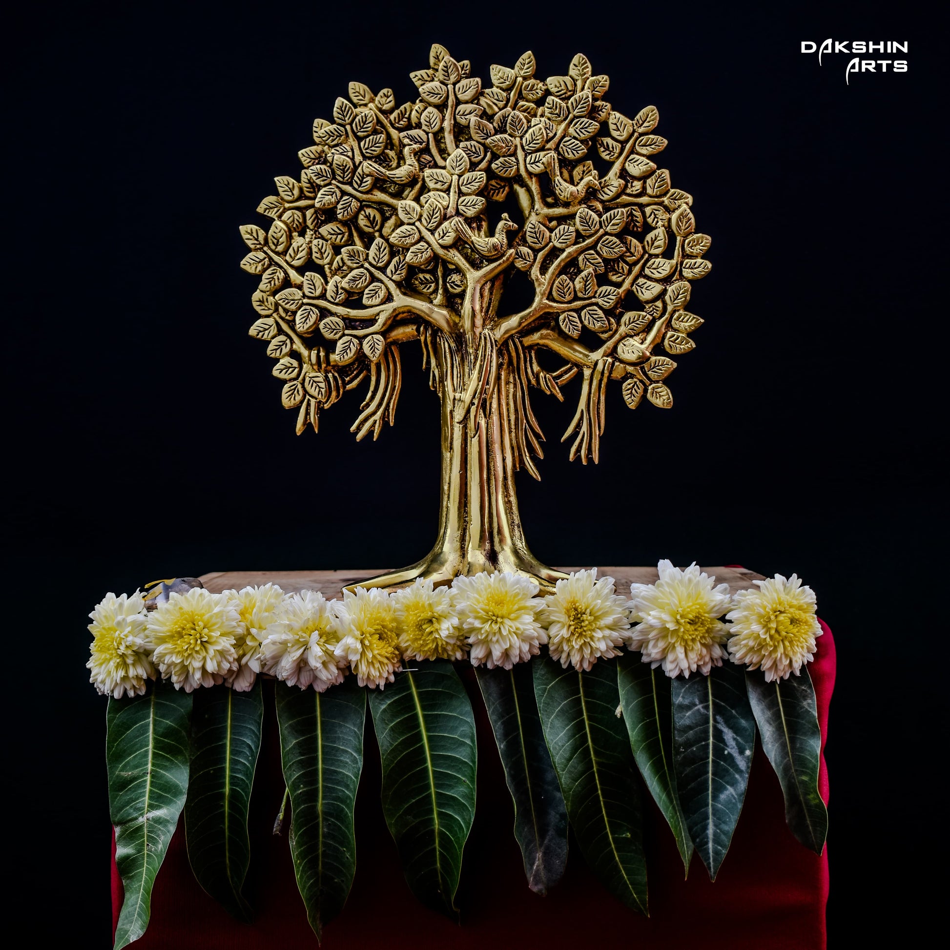 Golden tree sculpture with intricate leaves on dark background, adorned with white and yellow flowers and green leaves- Dakshin Arts