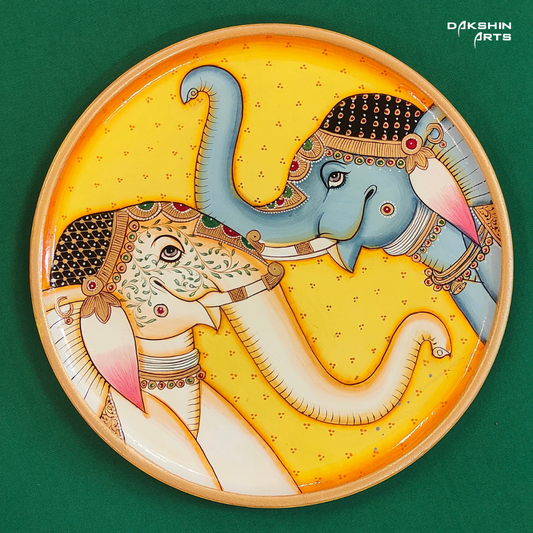 A decorative Pichwai wooden plate features two intricately painted elephants facing each other on a yellow background - Dakshin Arts