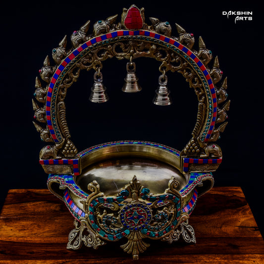 Ornate and colorful brass stonework urli with intricate designs, featuring three silver bells hanging in the arch - Dakshin Arts