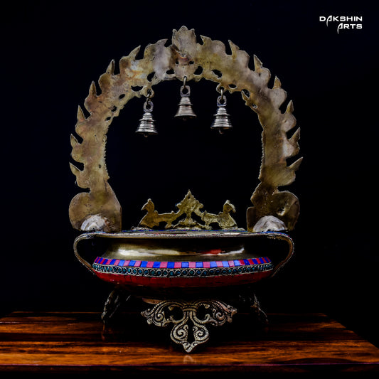 Ornate and colorful brass stonework urli with intricate designs, featuring three silver bells hanging in the arch - Dakshin Arts