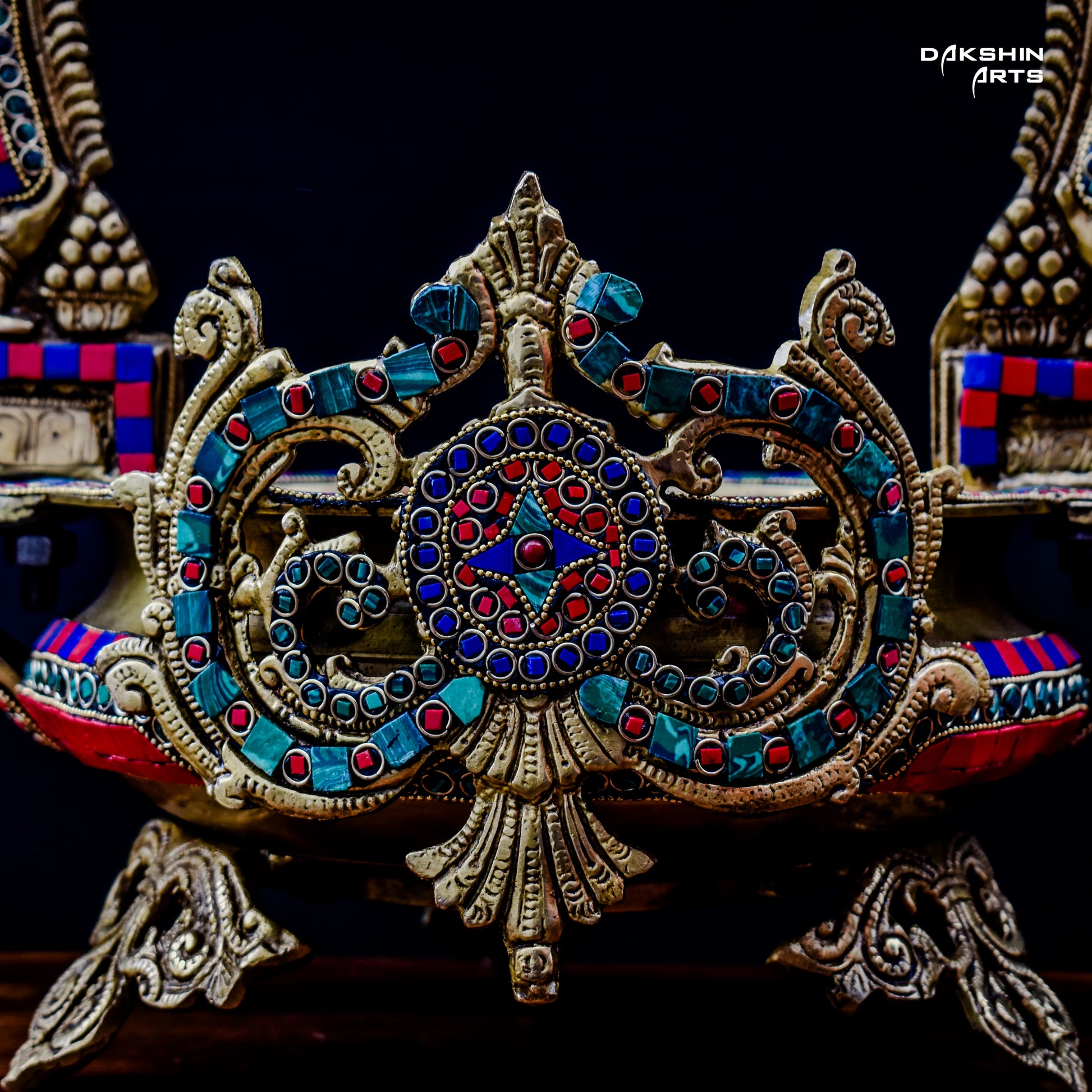 Ornate and colorful brass stonework urli with intricate designs, featuring three silver bells hanging in the arch - Dakshin Arts