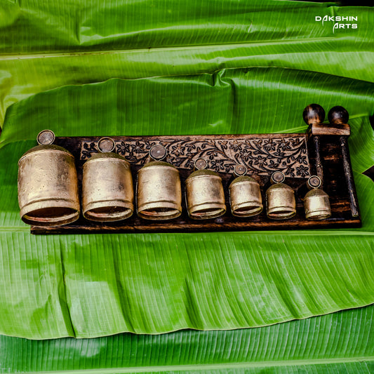 Ornate brass coloured bell like pieces arranged by size on carved wooden stand - Dakshin Arts
