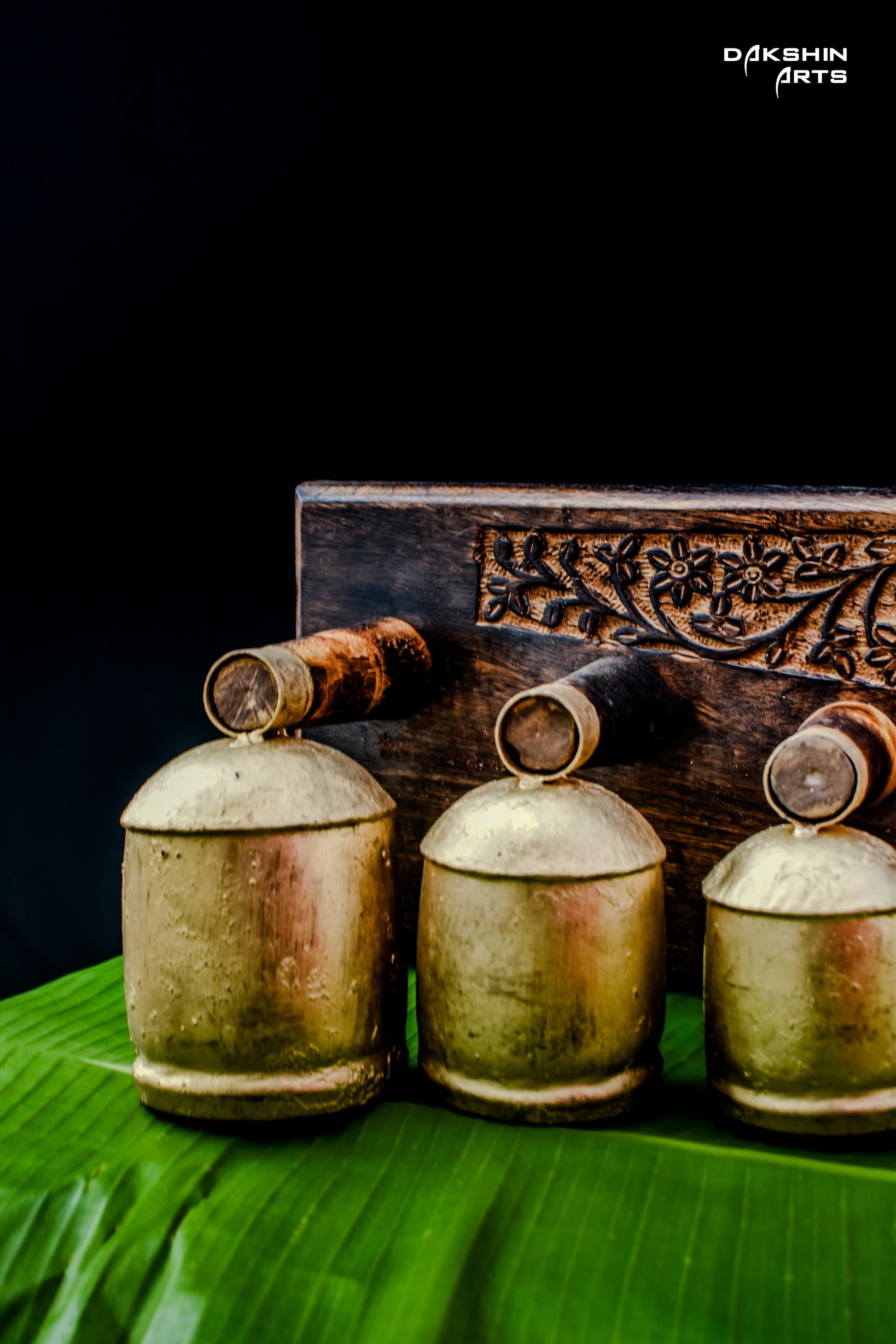 Ornate brass coloured bell like pieces arranged by size on carved wooden stand - Dakshin Arts