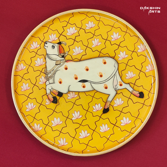 A decorative Pichwai wooden wall plate featuring a white cow on a vibrant yellow background with lotus - Dakshin Arts