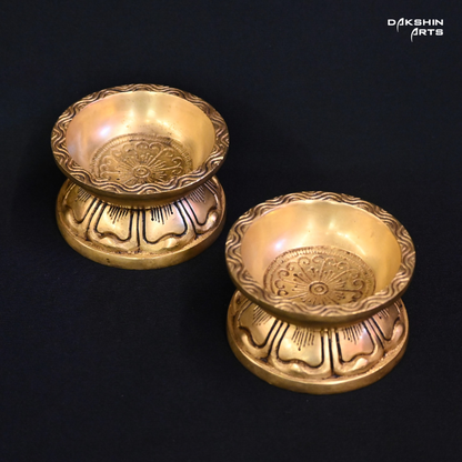 Two ornate brass diyas with engraved designs on a black background, exuding an elegant tone - Dakshin Arts