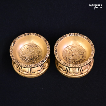 Two ornate brass diyas with engraved designs on a black background, exuding an elegant tone - Dakshin Arts