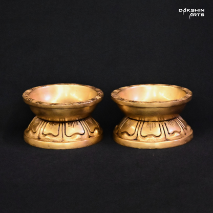 Two ornate brass diyas with engraved designs on a black background, exuding an elegant tone - Dakshin Arts