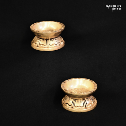 Two ornate brass diyas with engraved designs on a black background, exuding an elegant tone - Dakshin Arts