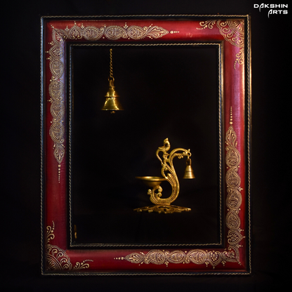 Ornate brass oil diya with intricate carvings, featuring a peacock design and a small hanging bell on a dark background - Dakshin Arts