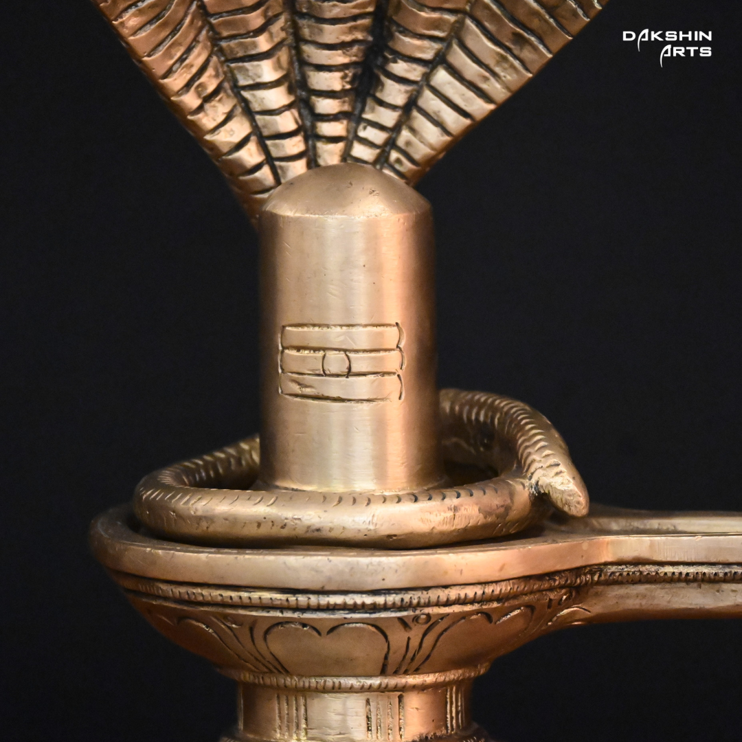 Brass sculpture of a Shivling with a five-headed cobra hood, set on a wooden surface against a black background- Dakshin Arts