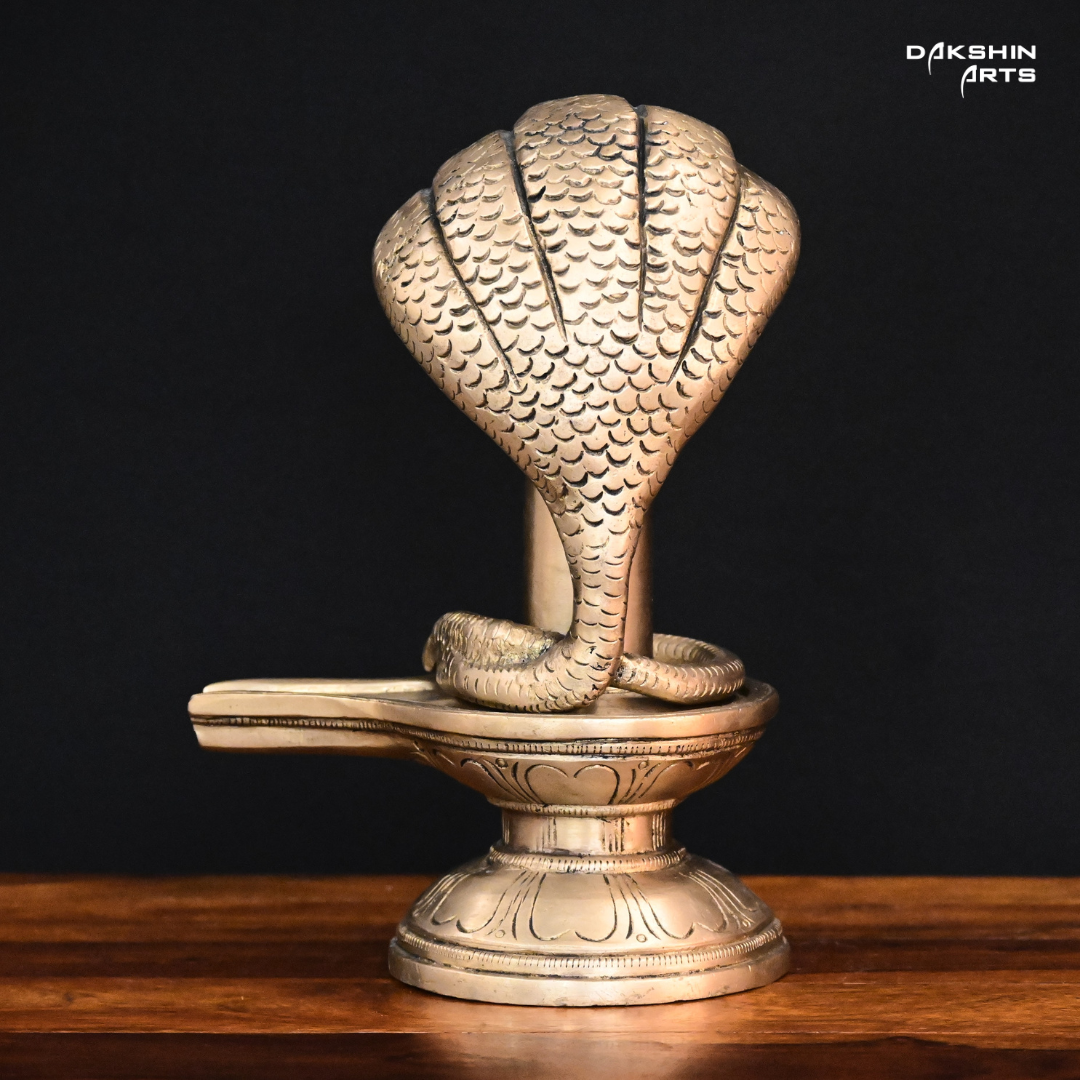 Brass sculpture of a Shivling with a five-headed cobra hood, set on a wooden surface against a black background- Dakshin Arts