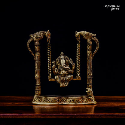 A brass Ganesha statue on a decorative swing with intricate bird carvings - Dakshin Arts