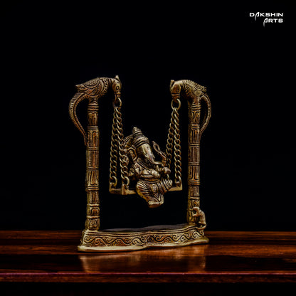 Side view of a brass Ganesha statue on a decorative swing with intricate bird carvings - Dakshin Arts