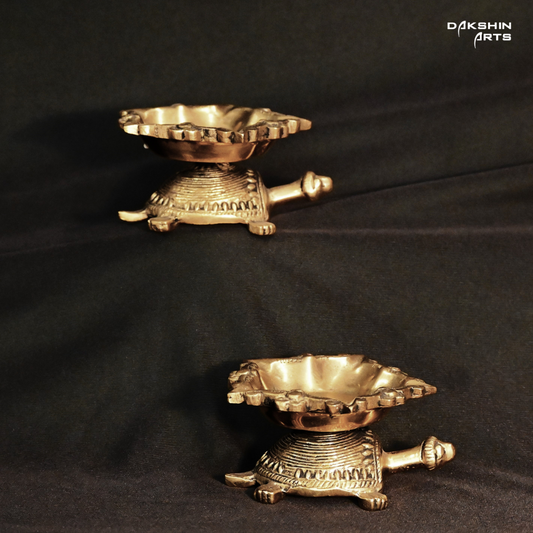 A brass decorative piece in the shape of a turtle with a diya on top.